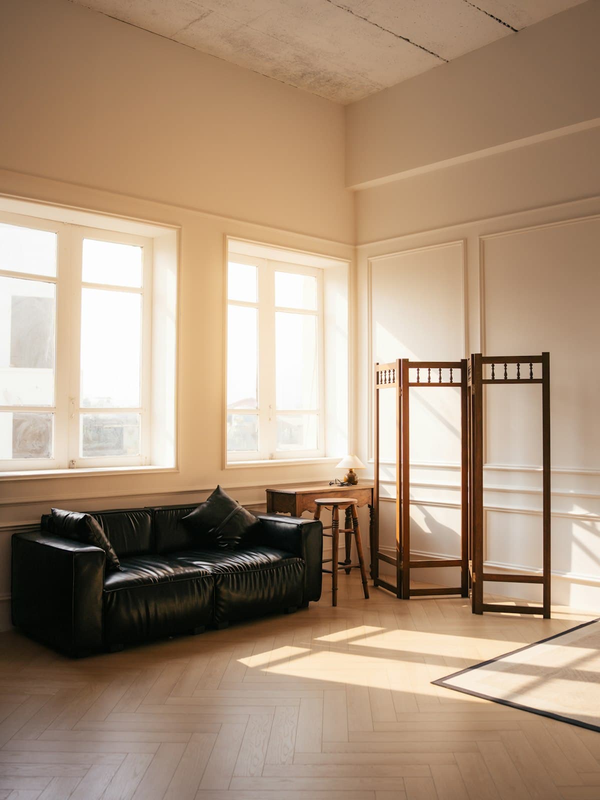 A sunlit room with herringbone parquet, tall windows and morning light across the floor.