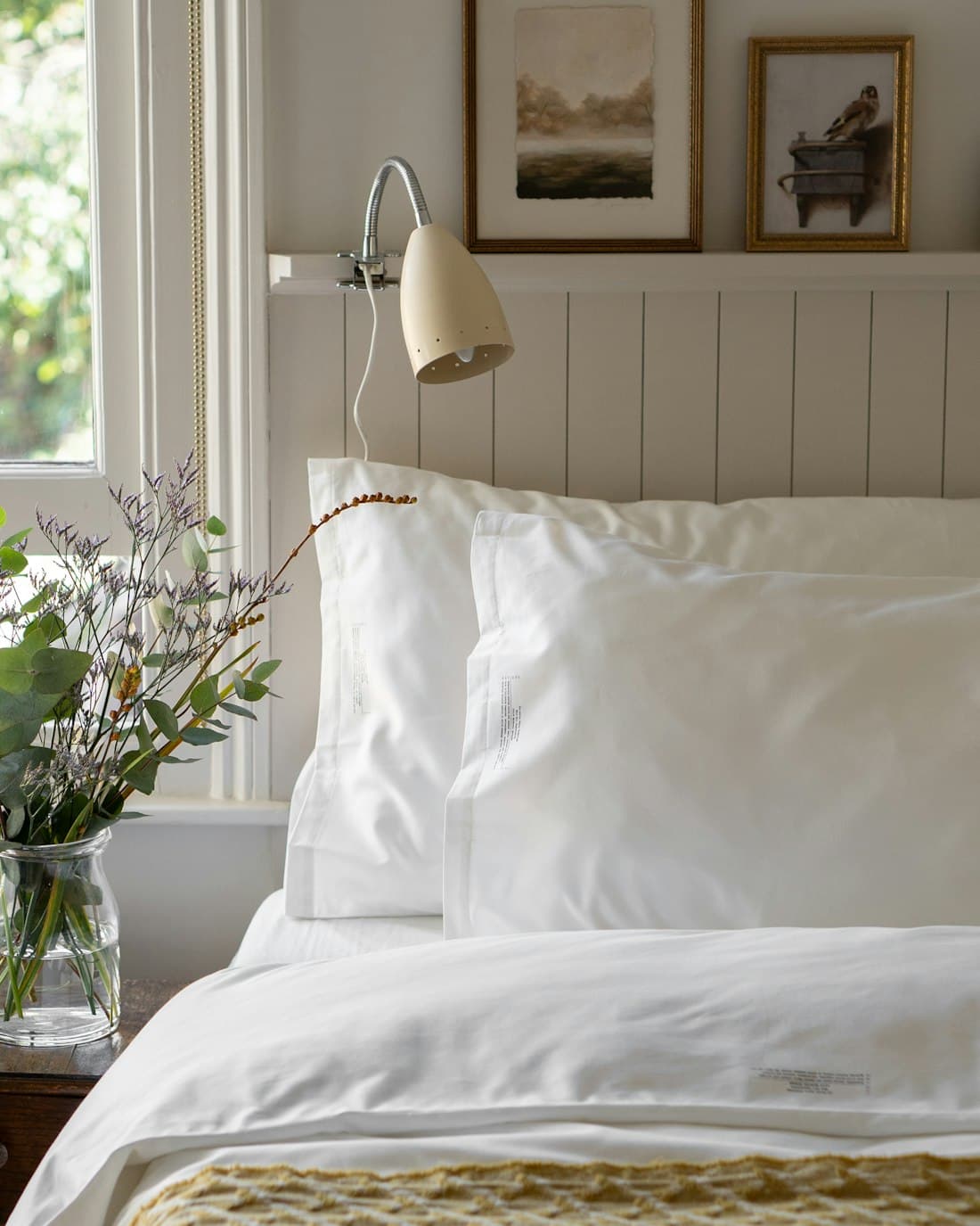 A made bed in white linen beside a window, with daylight falling across the room.