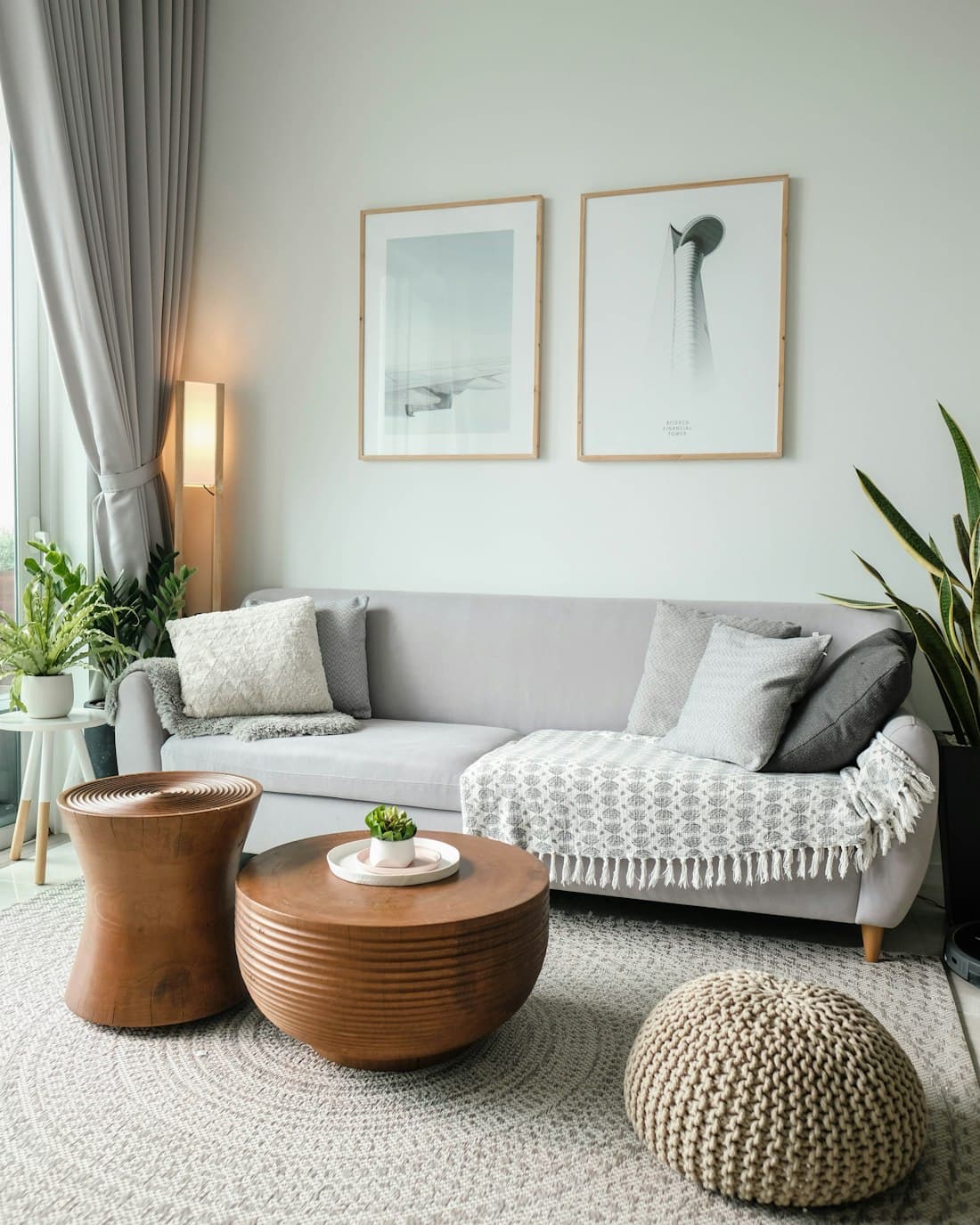 A bright living room with wooden furniture, linen textiles and daylight from a tall window.